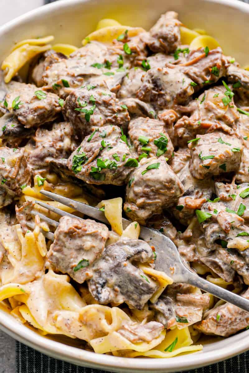close up of crockpot beef stroganoff in a white bowl with a fork.