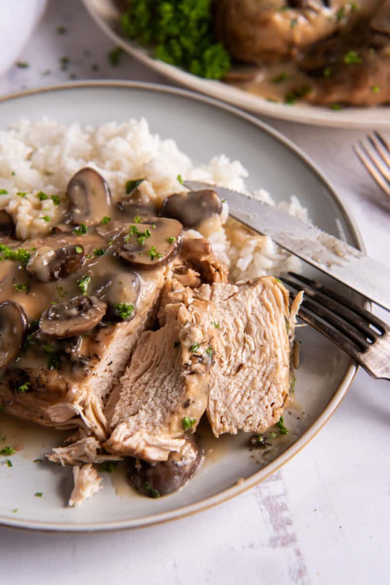 sliced crockpot chicken marsala with white rice on a white plate.