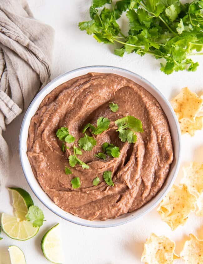 crockpot refried beans in a white bowl with cilantro.