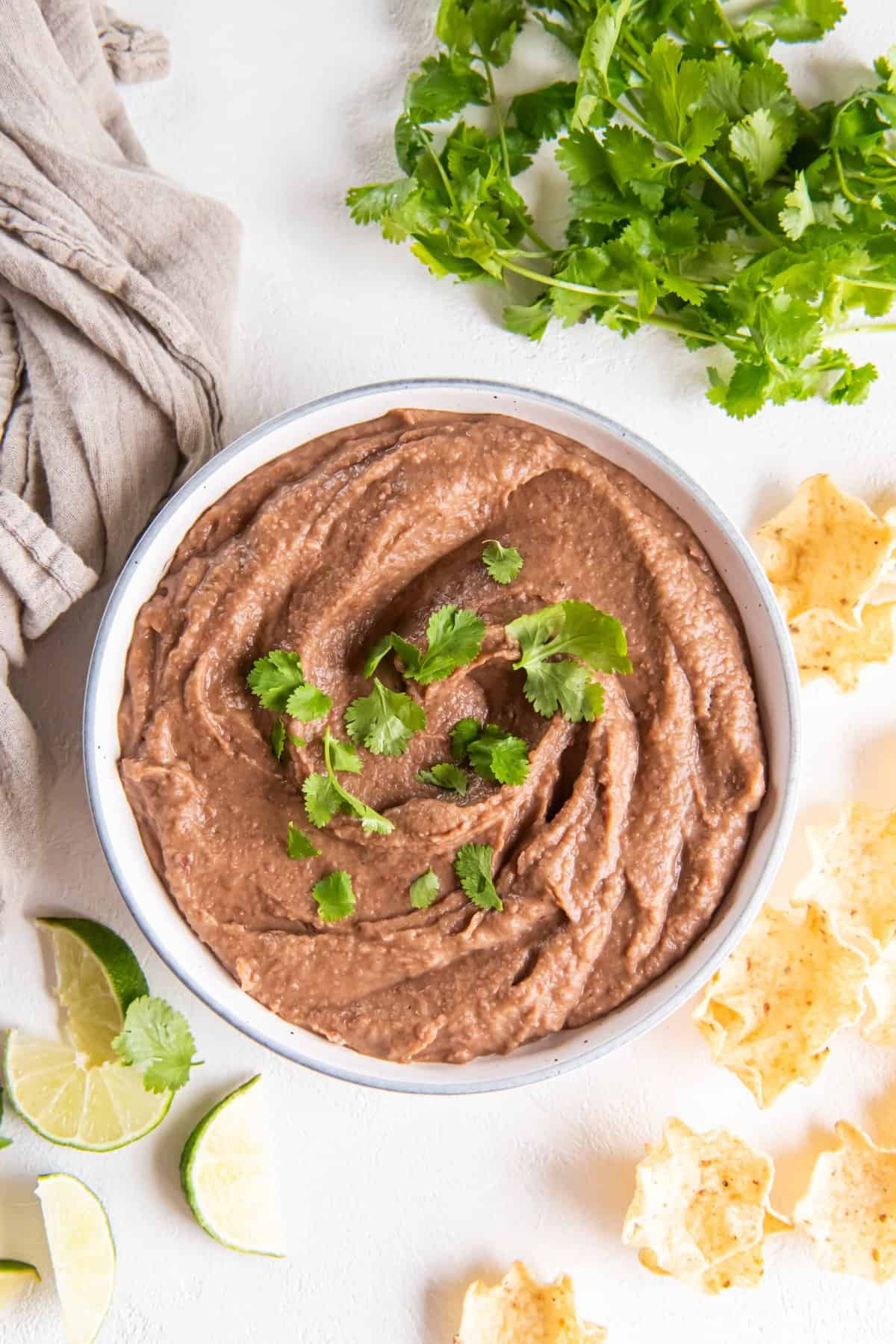 crockpot refried beans in a white bowl with cilantro.