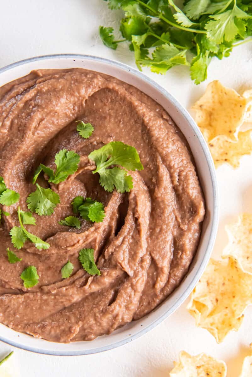 crockpot refried beans in a white bowl with cilantro.