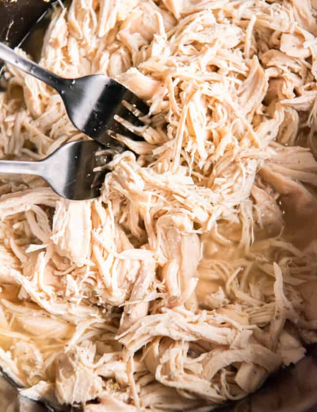 close up of shredded chicken in a crockpot with 2 forks.