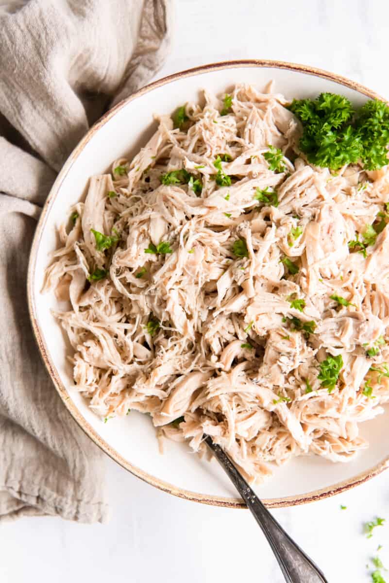 crockpot shredded chicken in w white bowl with a fork.