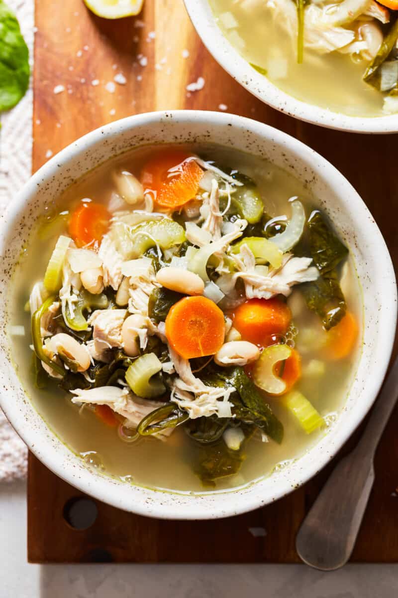 Tuscan Chicken Soup is something that you can enjoy year-round. This crockpot chicken soup recipe is so delicious and so simple. An easy Tuscan Soup to make at home, filled with so many good ingredients. bowl of chicken soup with beans, spinach, and carrots