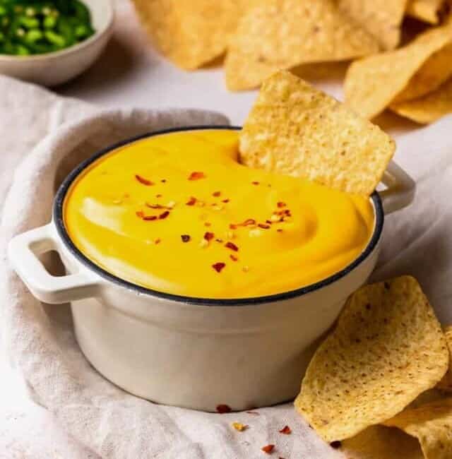 bowl of nacho cheese with tortilla chips dipped in it