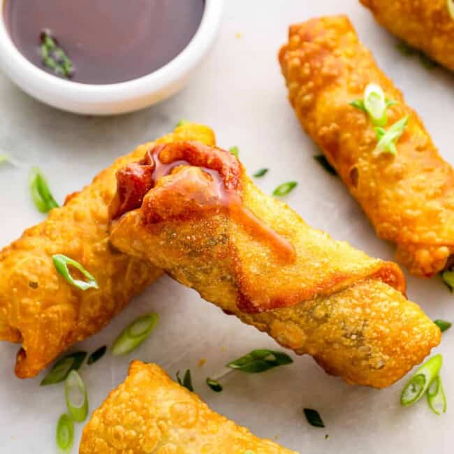 5 egg rolls on a white plate with dipping sauce.