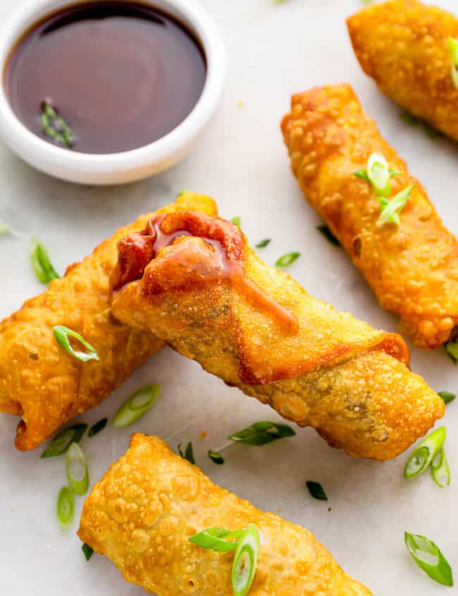 5 egg rolls on a white plate with dipping sauce.