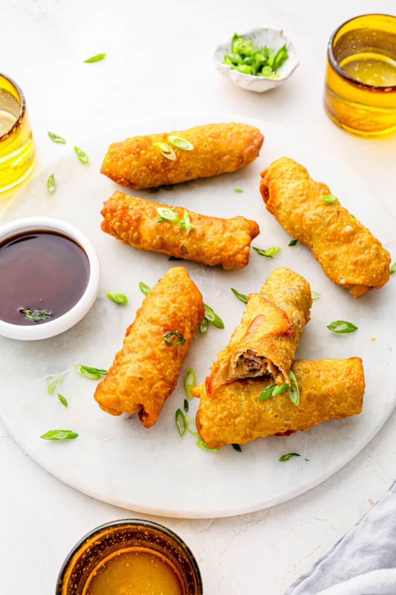 6 egg rolls on a white plate with dipping sauce.