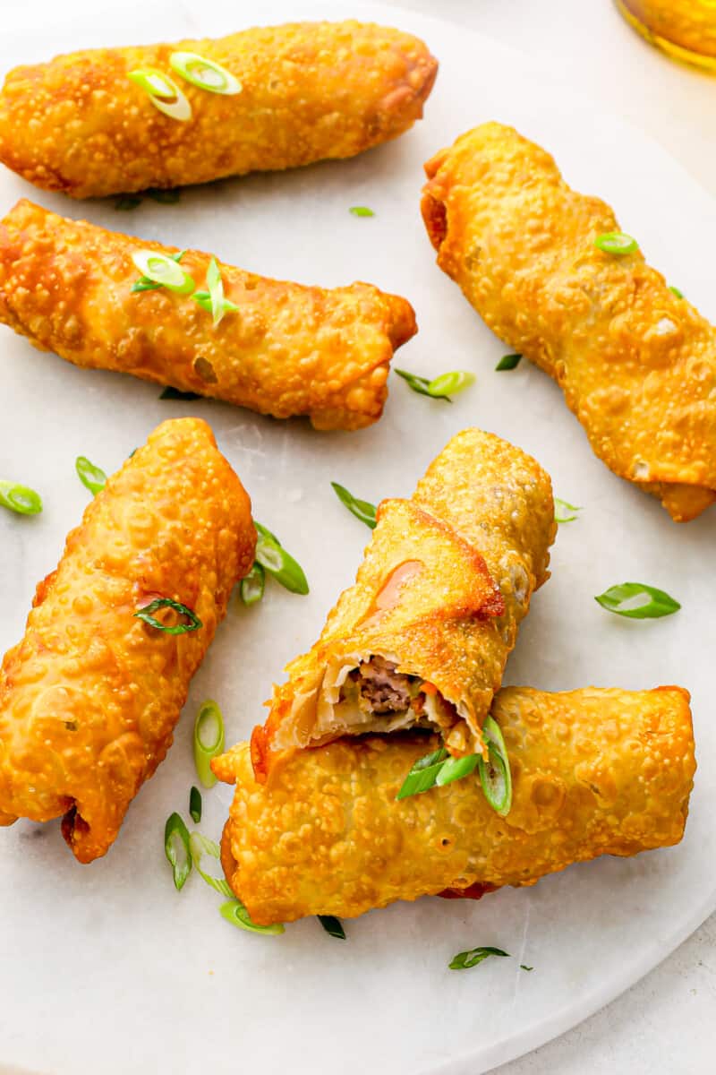 bitten egg roll resting on a white plate with 5 egg rolls.