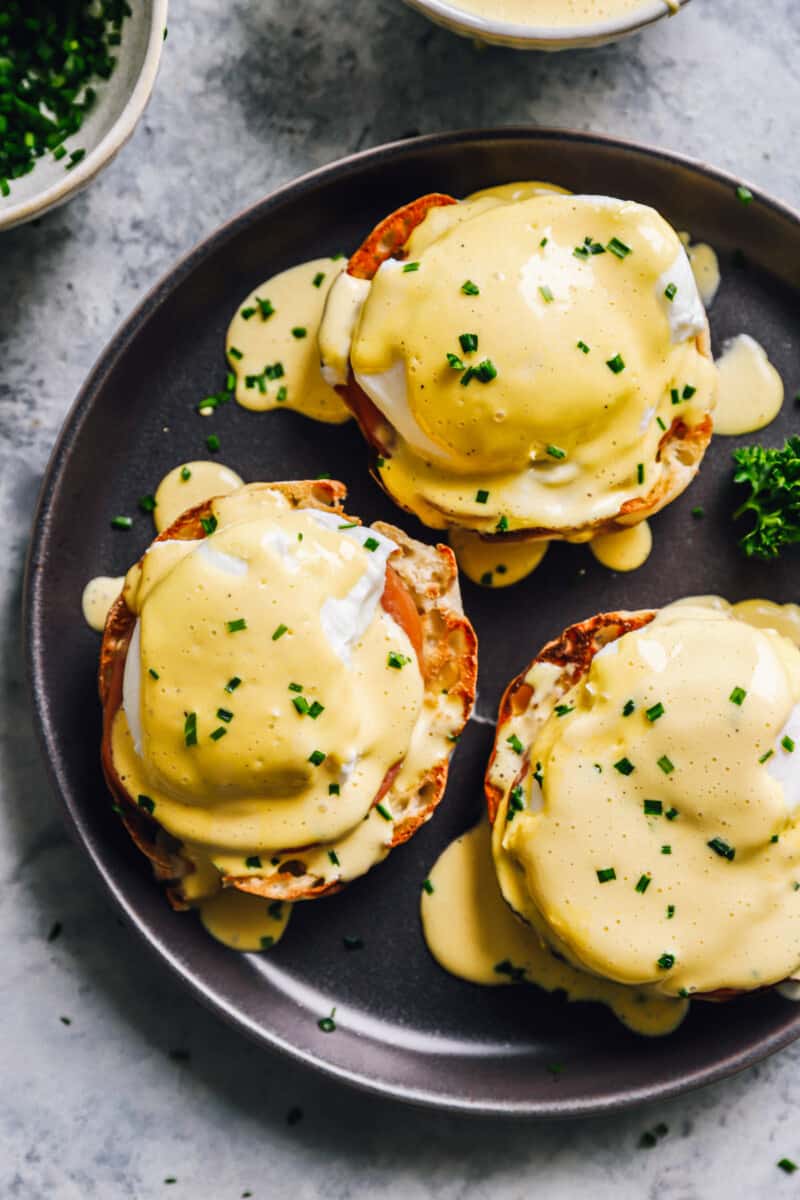 3 eggs benedict on a black plate.