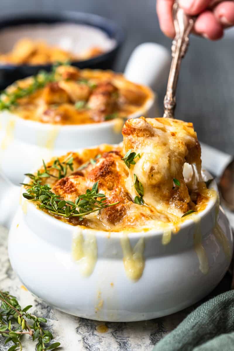 a spoonful of french onion soup hovering over french onion soup in a white bowl.
