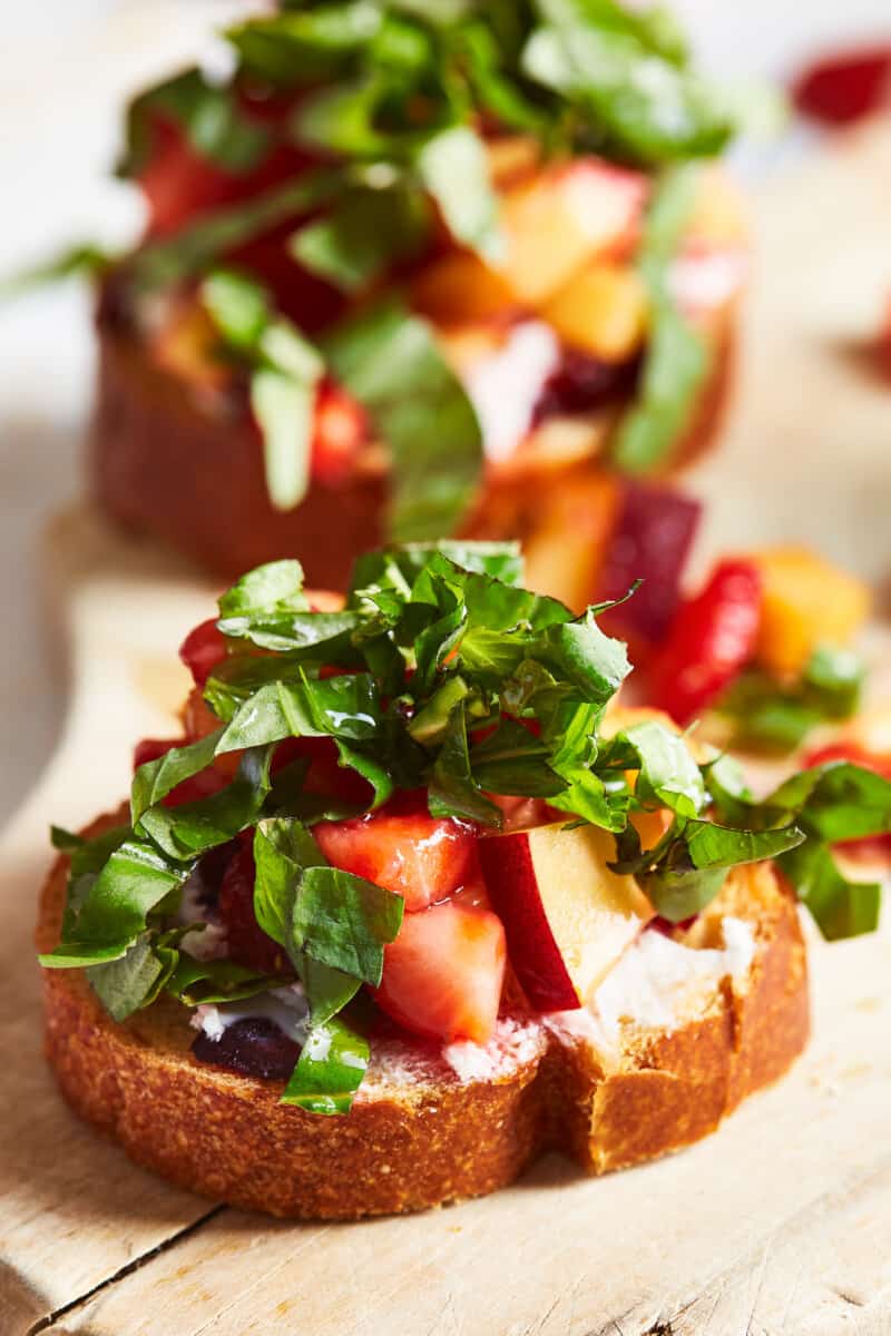 close up on piece of bruschetta with goat cheese, fruit, and basil