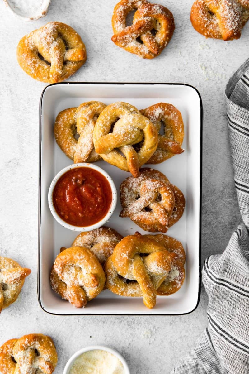 8 garlic parmesan soft pretzels in a white serving tray with marinara sauce.