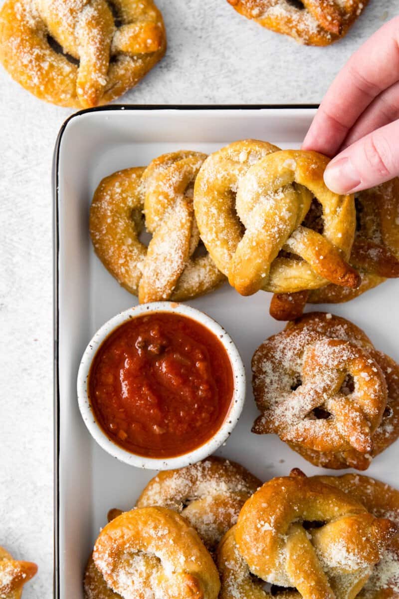 8 garlic parmesan soft pretzels in a white serving tray with marinara sauce.