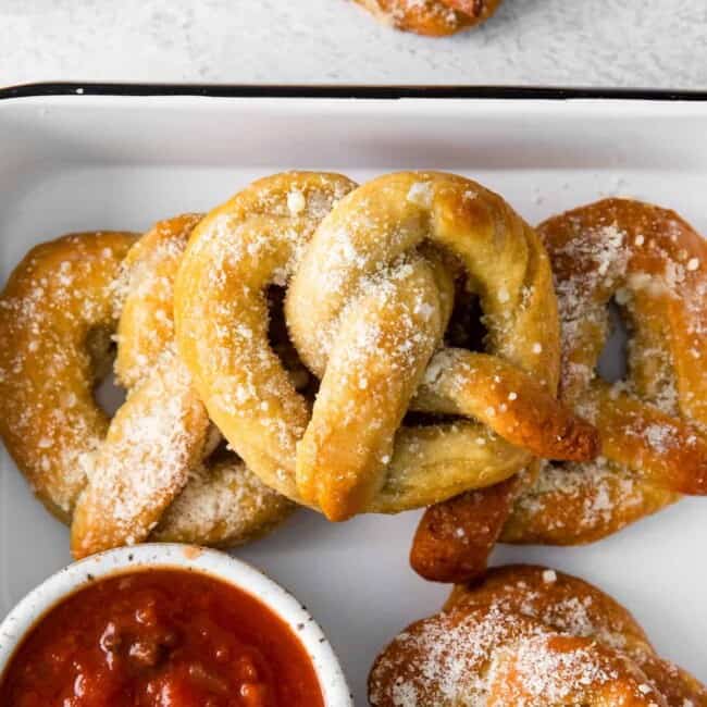 close up of garlic parmesan soft pretzels in a white serving tray with marinara sauce.