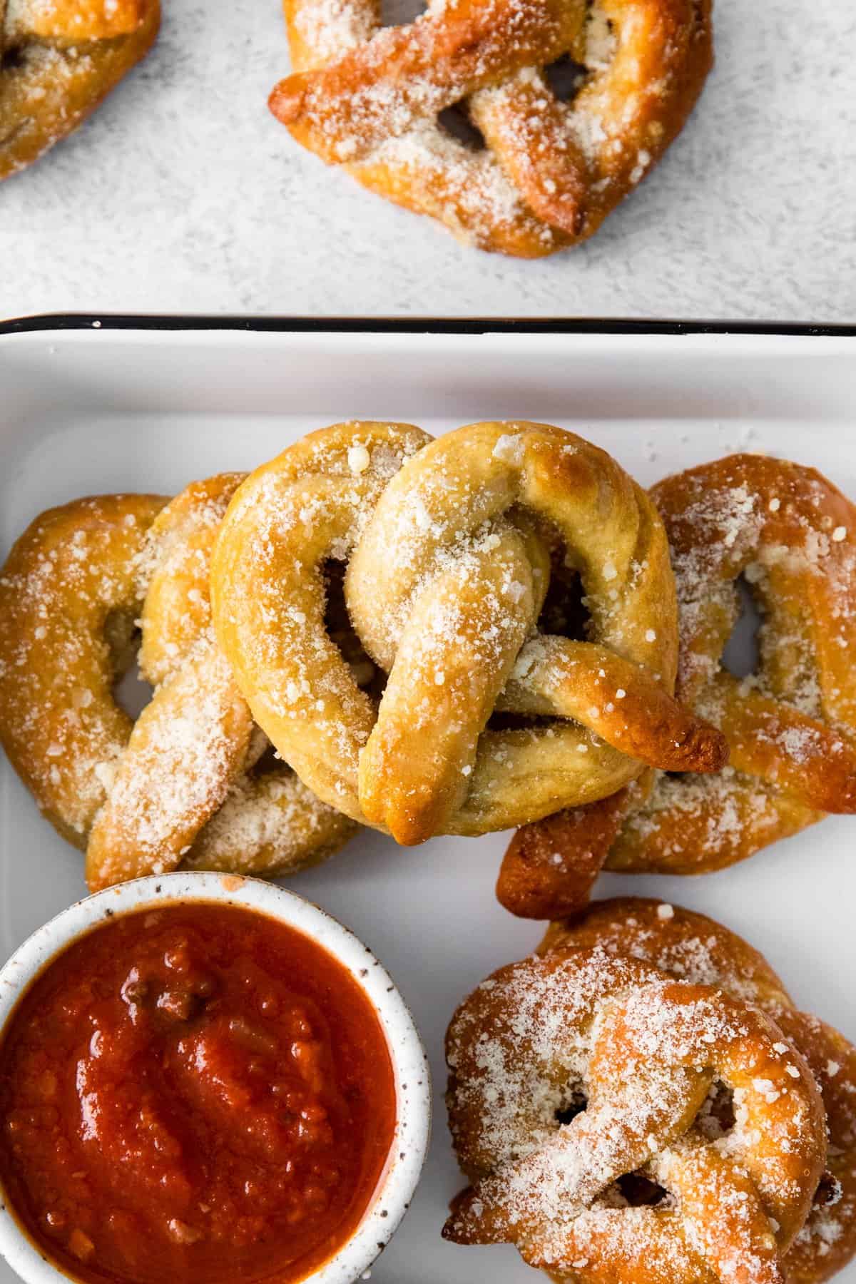 close up of garlic parmesan soft pretzels in a white serving tray with marinara sauce.