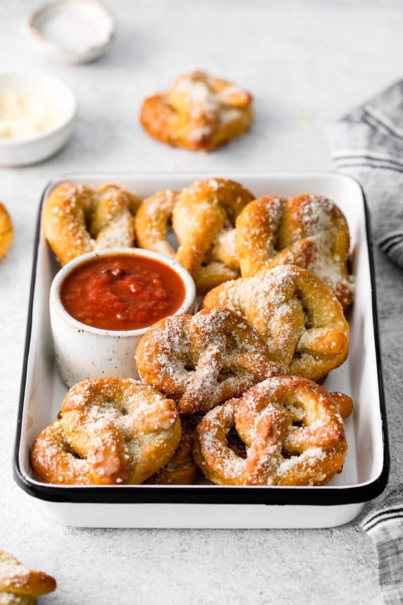 garlic parmesan soft pretzels piled into a white serving tray with marinara sauce.