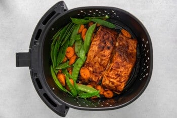 salmon carrots and snap peas in an air fryer basket.