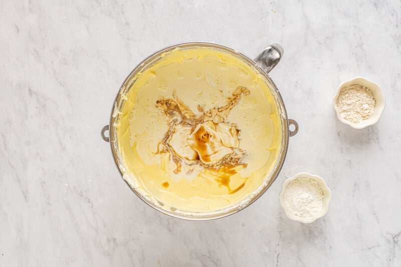 sour cream heavy cream and vanilla added to cheesecake batter in a stainless mixing bowl.