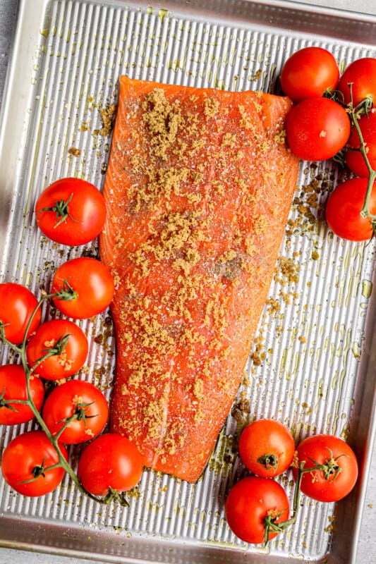 raw salmon filet on a baking tray with tomatoes on vines