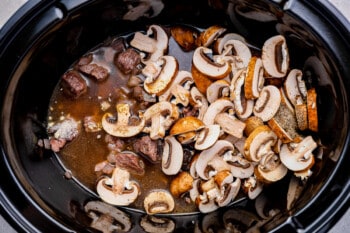 mushrooms and seasonings added to beef and onions in a crockpot.