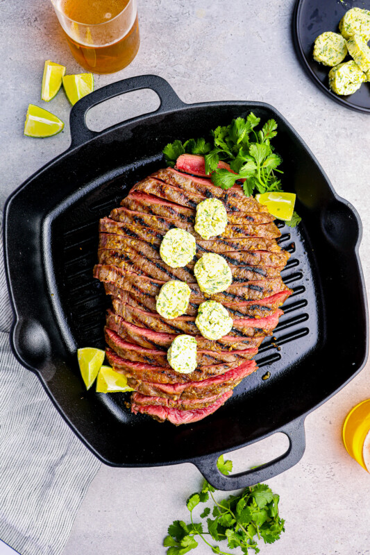 sliced flank steak on a grill pan topped with cilantro lime butter