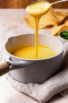 cheese sauce pouring out of a spoon into a pot of cheese sauce