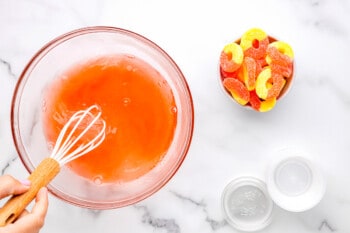 water and peach jello whisked together in a glass bowl with a whisk.