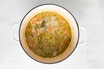 chicken stock corn and bay leaf added to vegetables in a dutch oven.