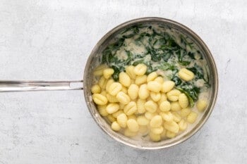 gnocchi added to spinach and parmesan cream sauce in a skillet.