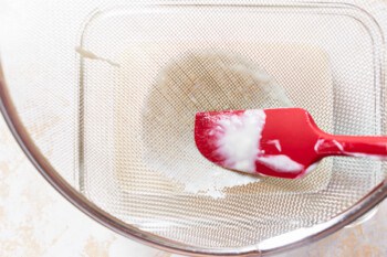 rubber spatula pushing milk and flour mixture through a strainger
