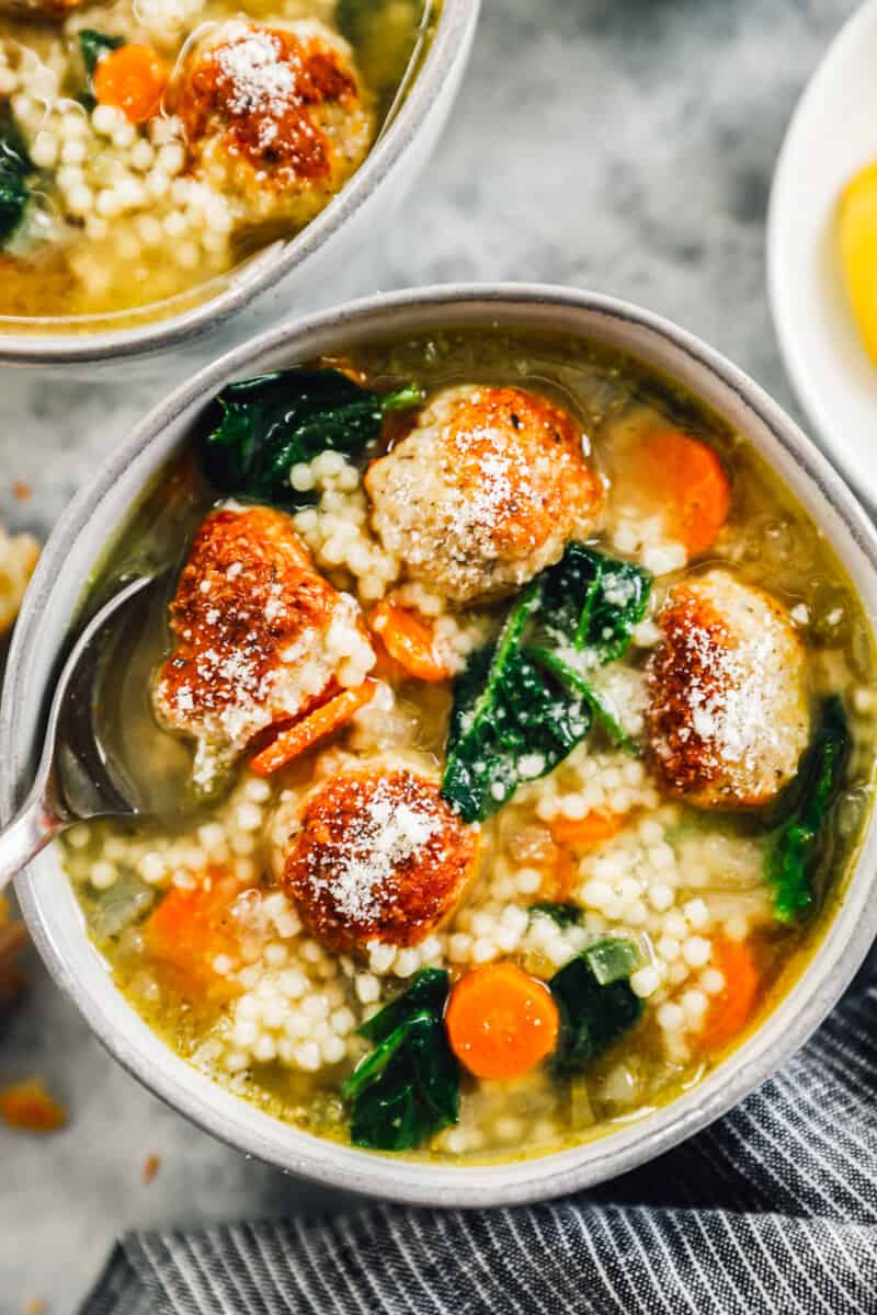 bowl of italian wedding soup filled with vegetables, couscous, and meatballs