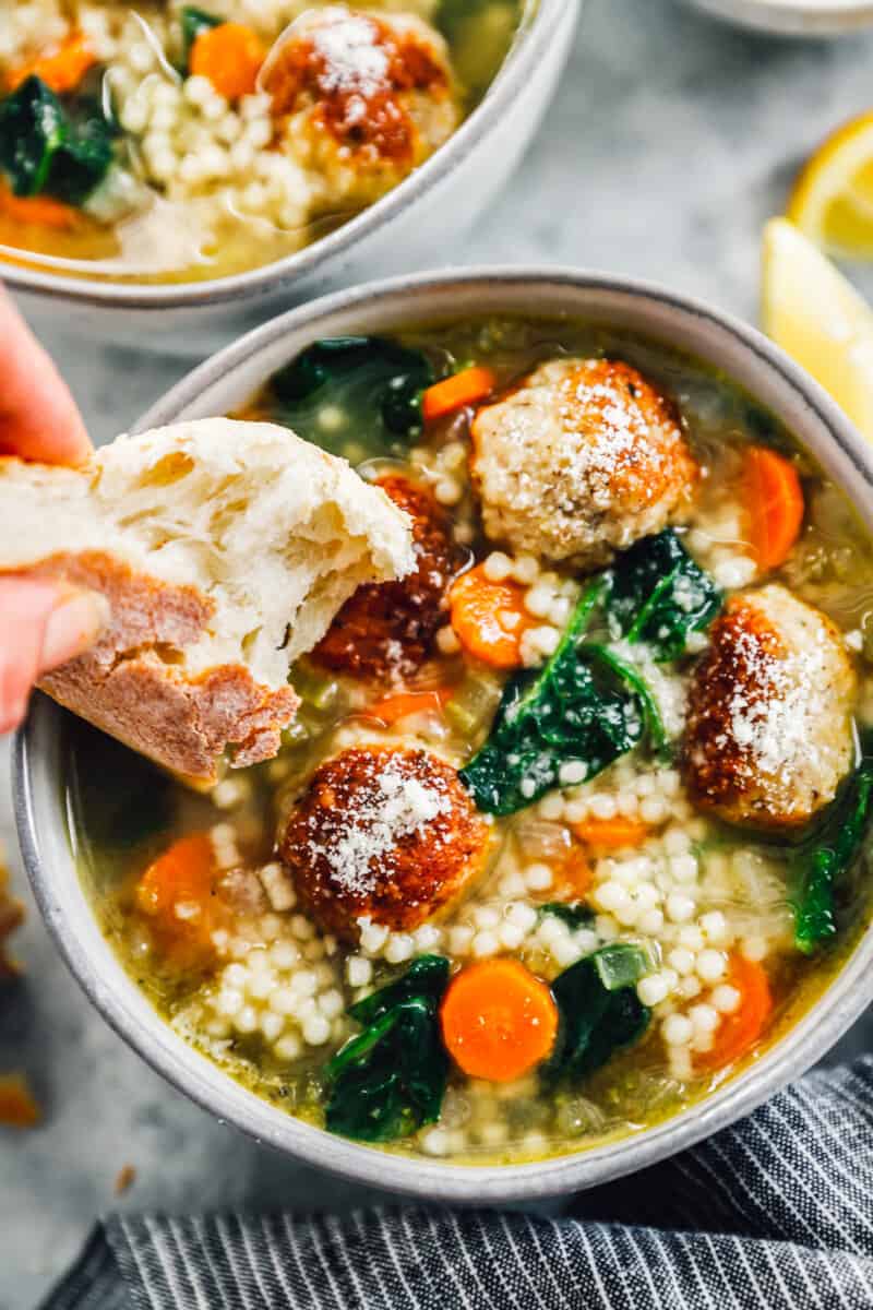 dipping a piece of bread into italian wedding soup