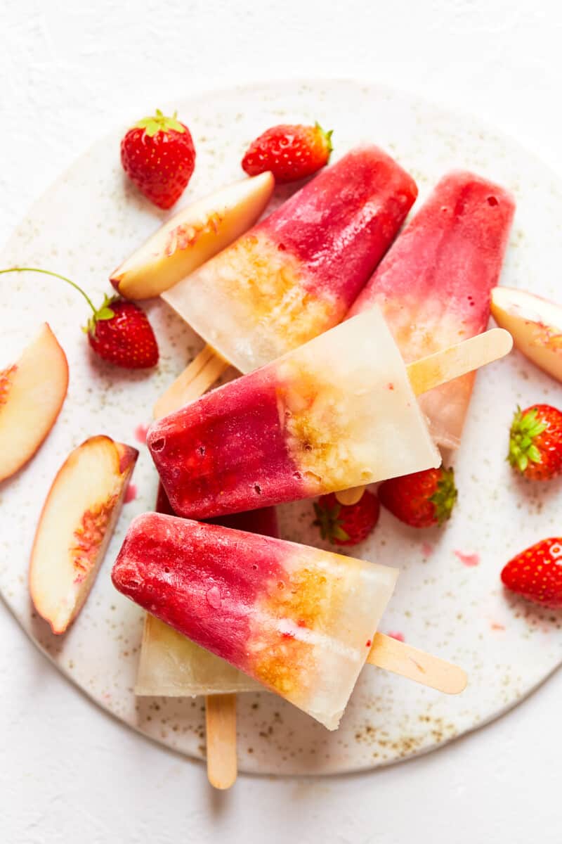 alcoholic margarita popsicles stacked up on a board with fresh strawberries and peaches