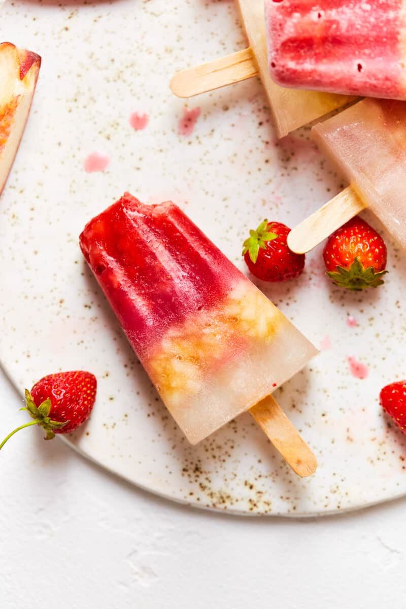 layered margarita popsicles on a board with strawberries