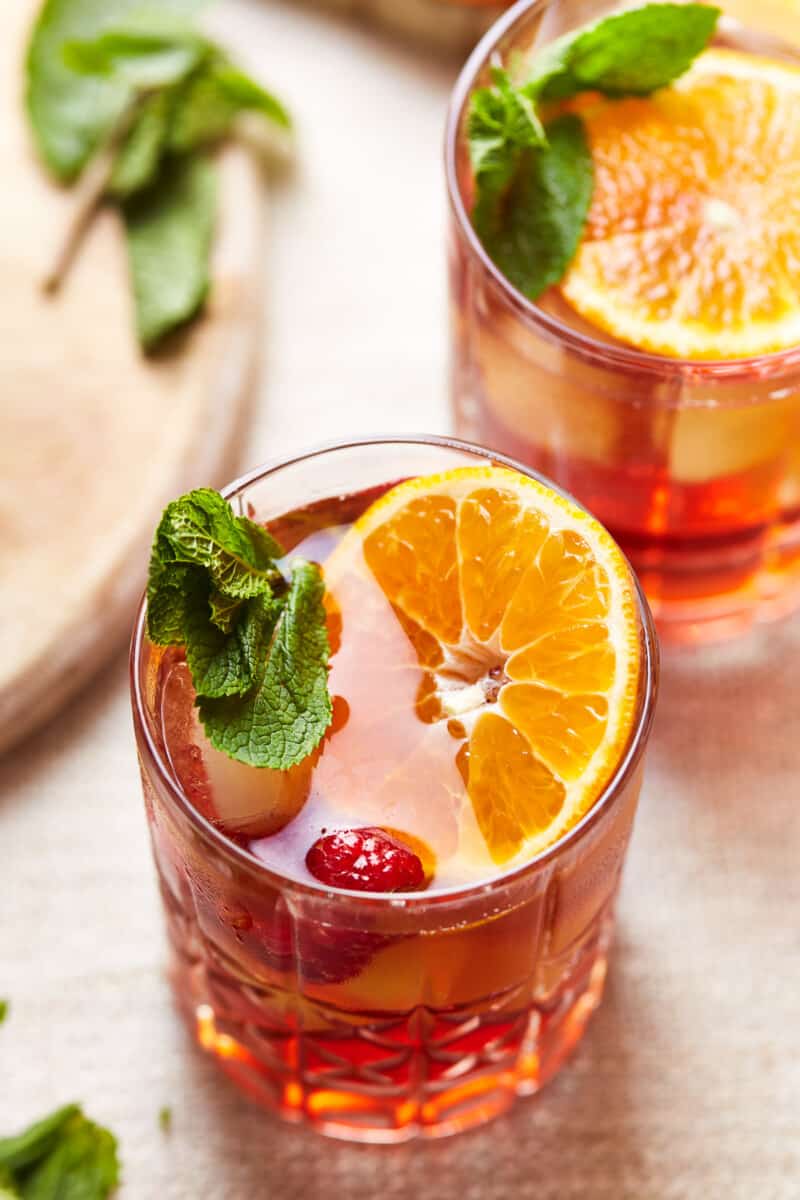 two glasses of spiked raspberry tea filled with fruit and mint