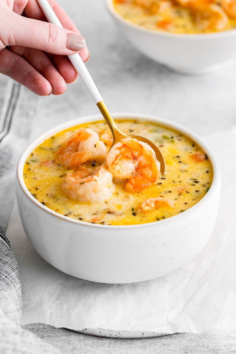 a spoon scooping a shrimp from shrimp corn chowder in a white bowl.