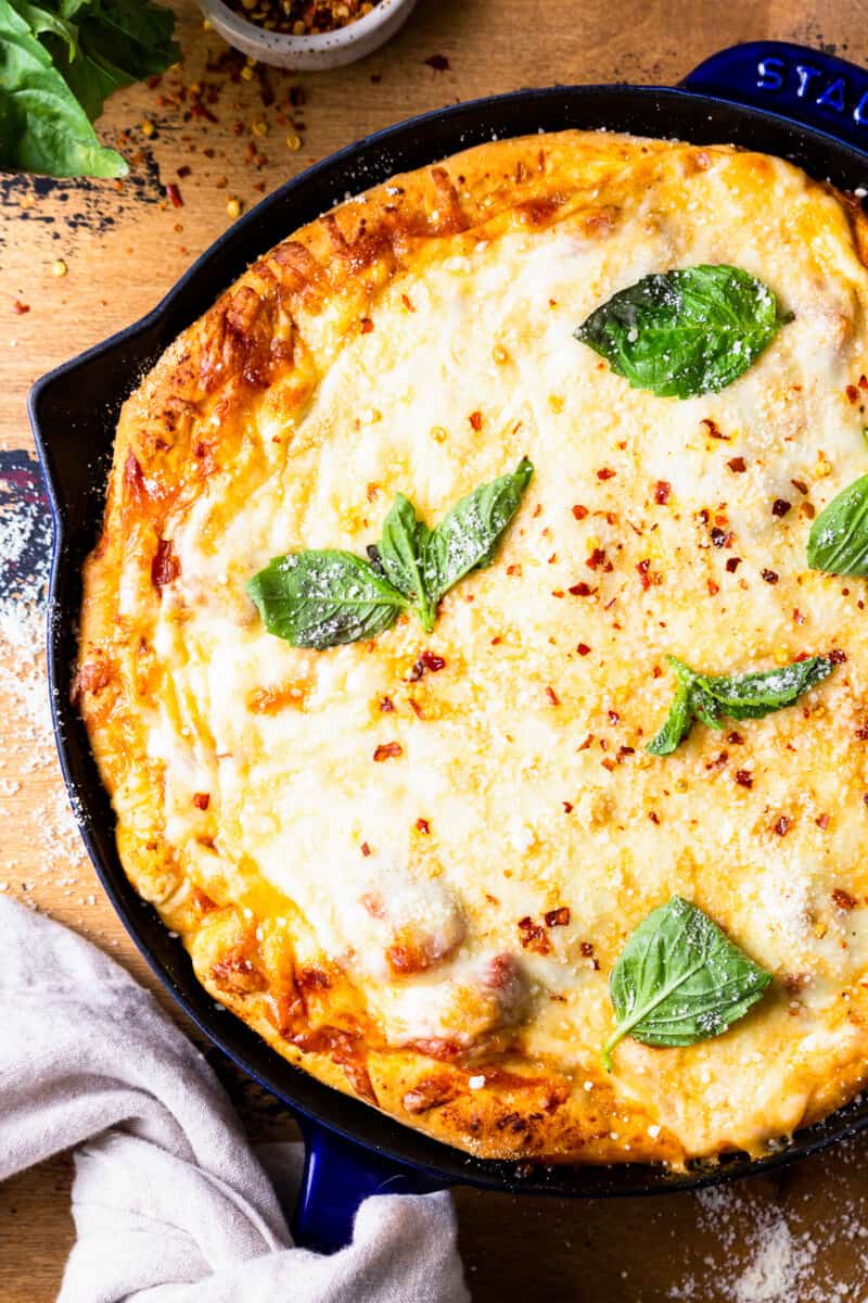 deep dish pizza topped with basil in a skillet