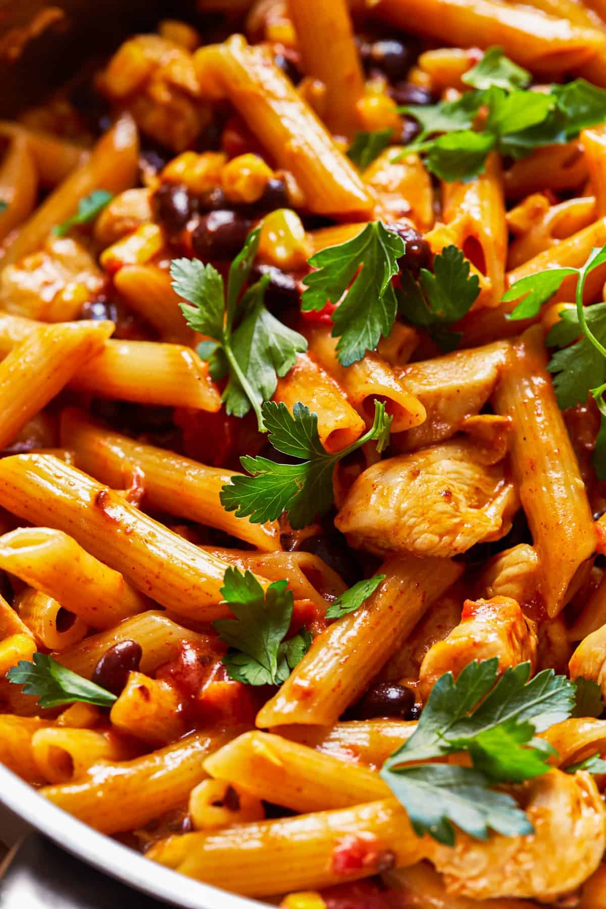 close up on skillet filled with penne pasta, chicken, black beans, and corn