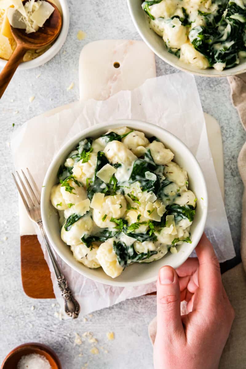 hand holding a bowl of parmesan spinach gnocchi.