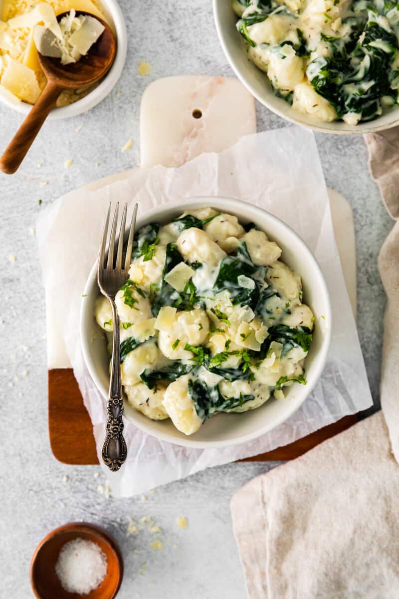 parmesan spinach gnocchi in a white bowl with a fork.