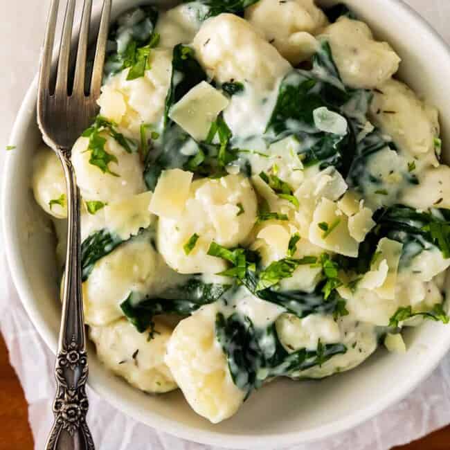 parmesan spinach gnocchi in a white bowl with a fork.