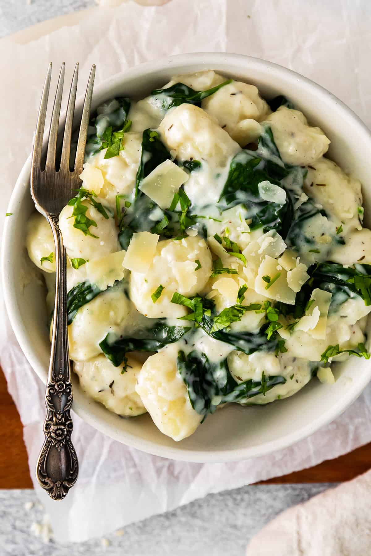 parmesan spinach gnocchi in a white bowl with a fork.