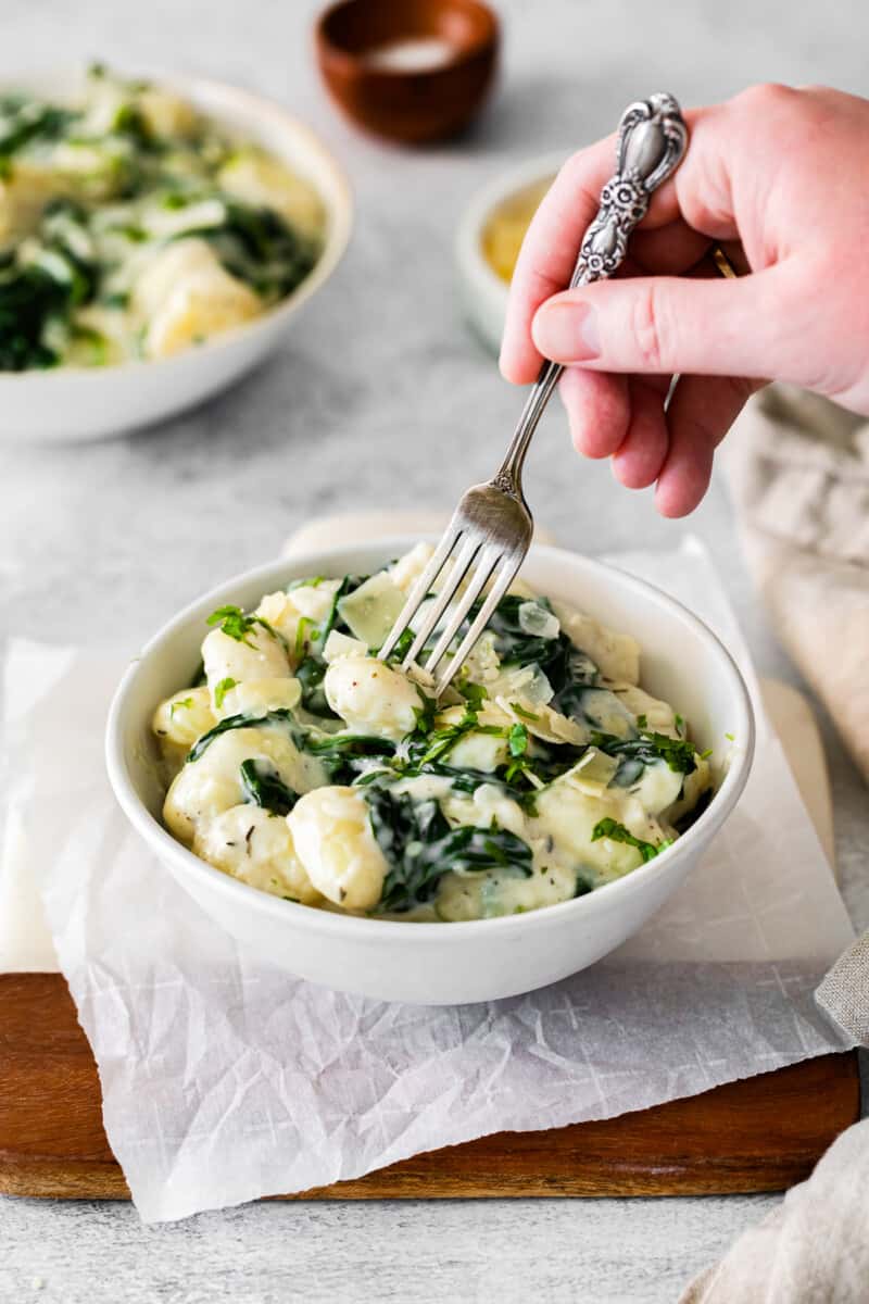 a fork stabbing a gnocchi from a bowl of parmesan spinach gnocchi.