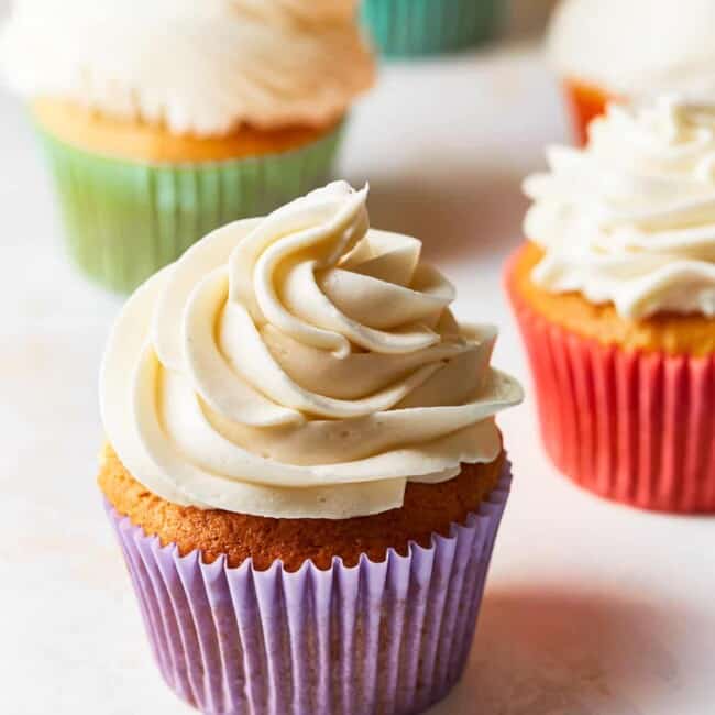 cupcakes topped with vanilla frosting, in different colored cupcake wrappers