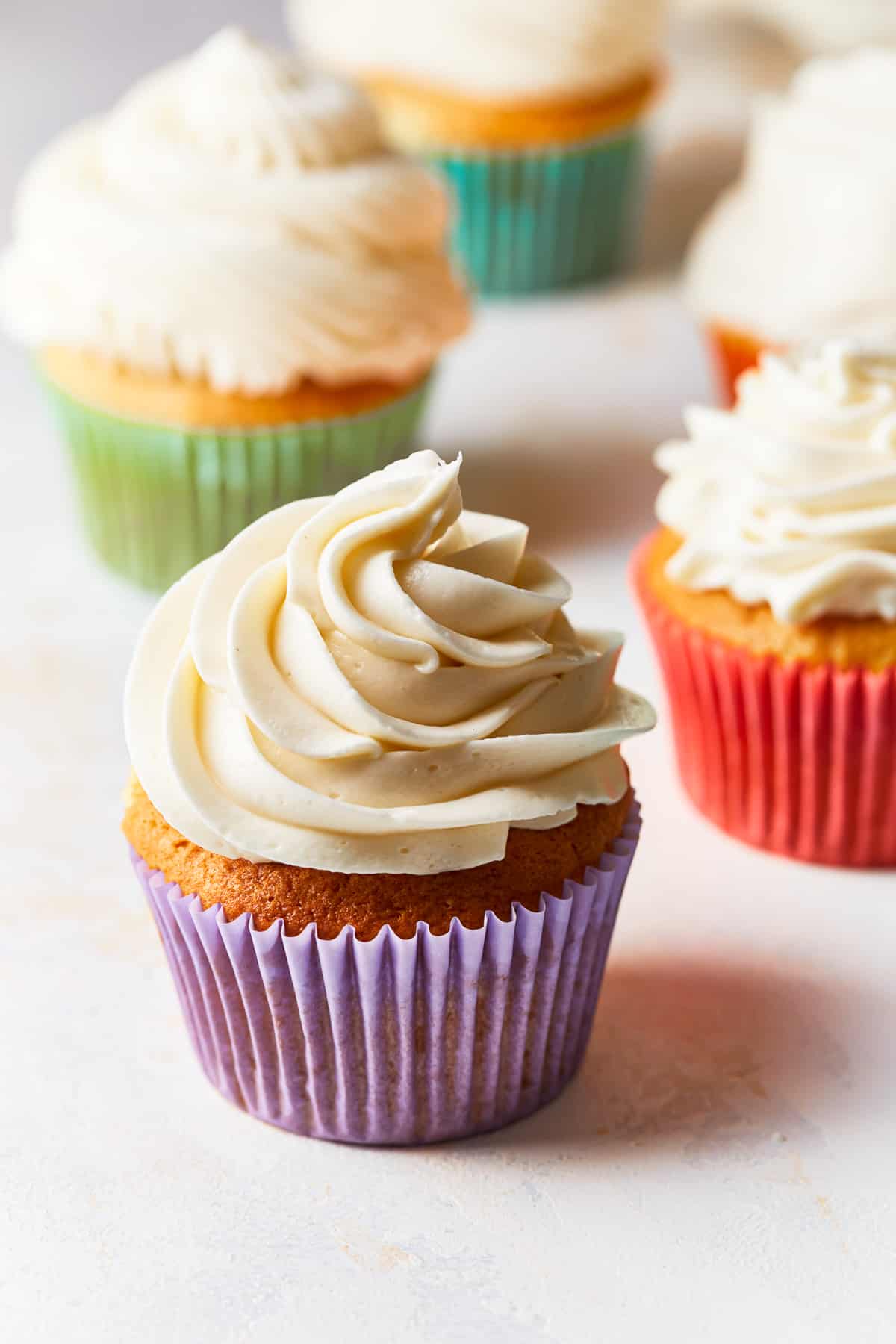 cupcakes topped with vanilla frosting, in different colored cupcake wrappers