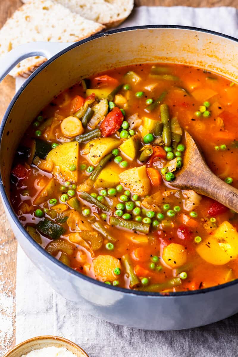 large pot filled with vegetable soup, with peas, potatoes, green beans, and more