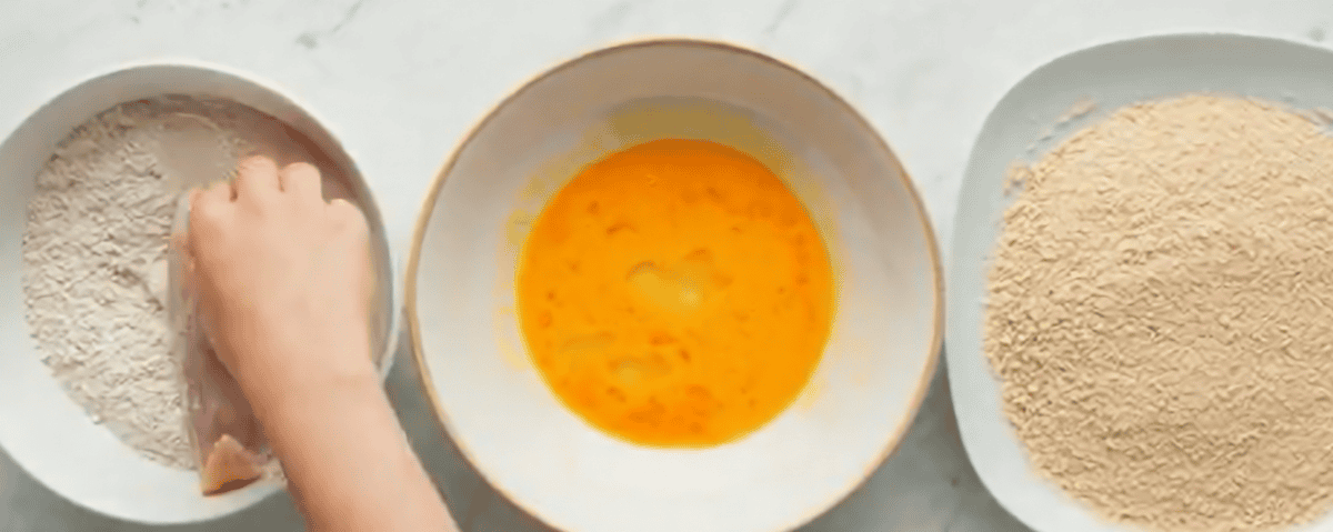 Dredging the chicken in flour with bowls of egg and breadcrumbs. 