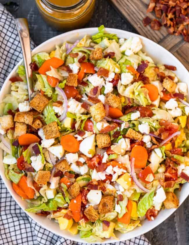 overhead view of chopped salad in a white serving bowl with a spoon.