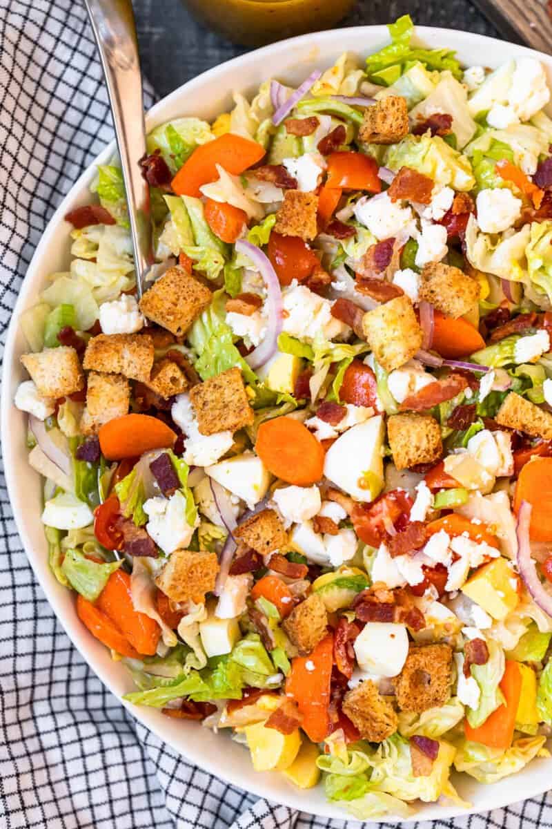 overhead view of chopped salad in a white serving bowl with a spoon.